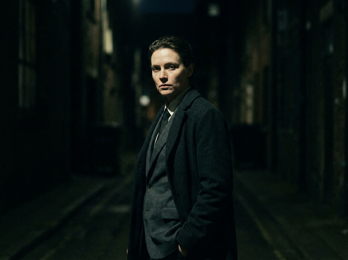 A figure in a sharp suit lit by a single hard key light, turning to camera mid-line