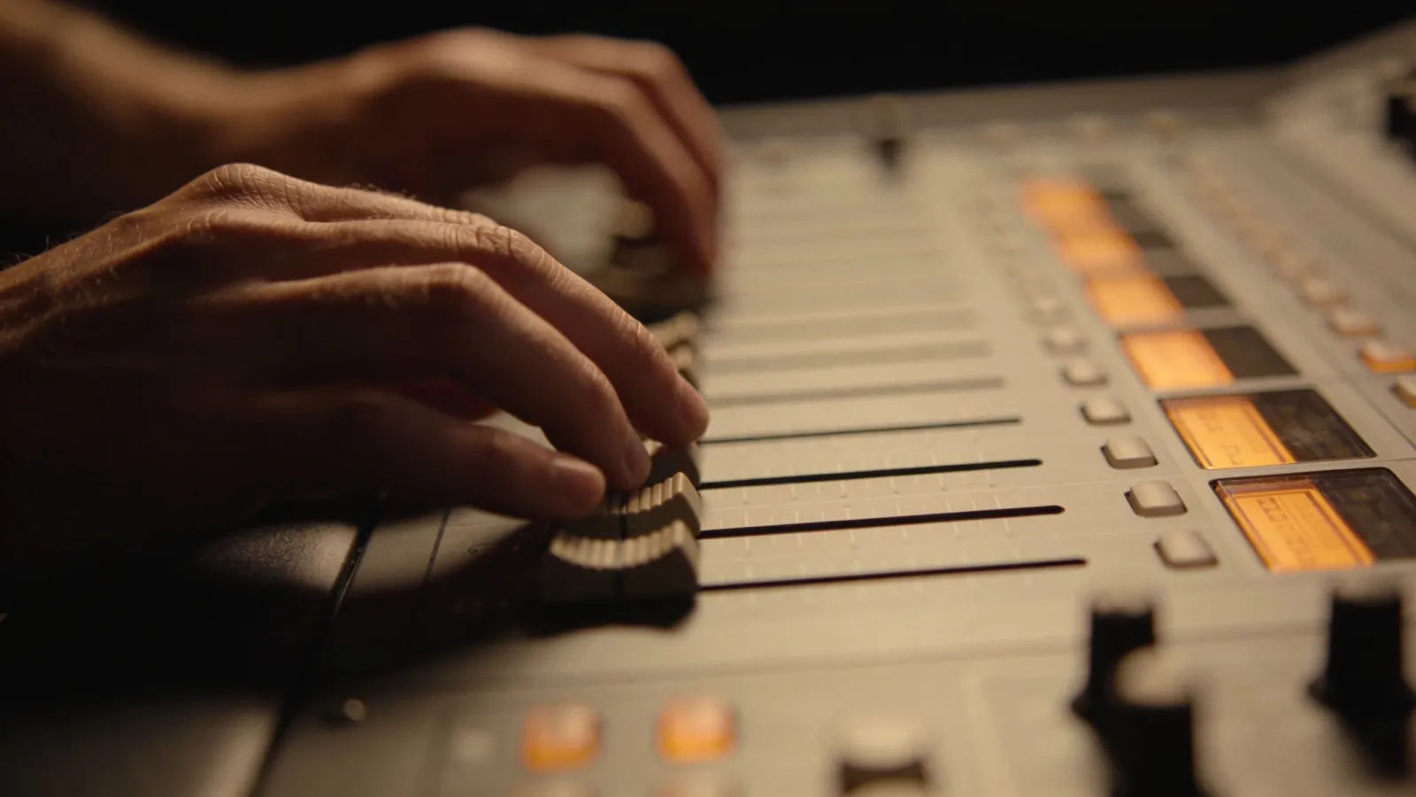 Hands on warm-lit console with amber audio UI