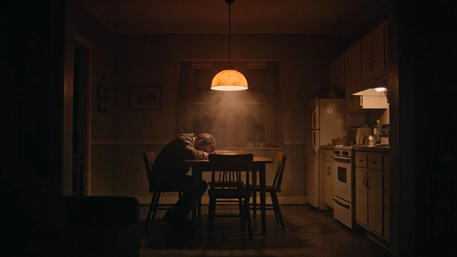 Weary figure slumped at late-night kitchen table