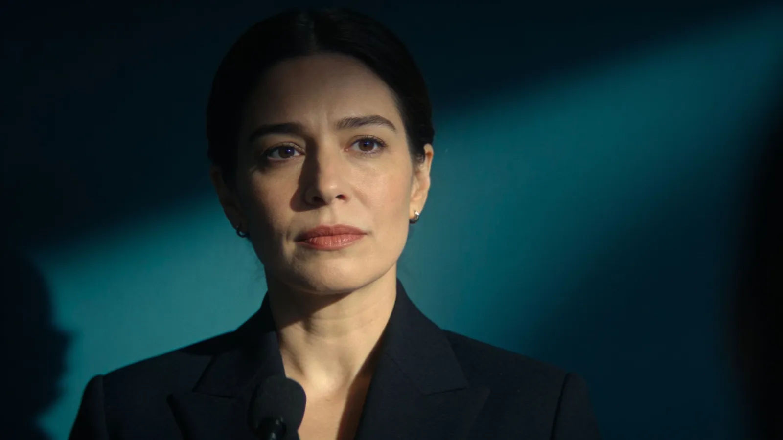 Poised commanding thought-leader mid-address in teal light