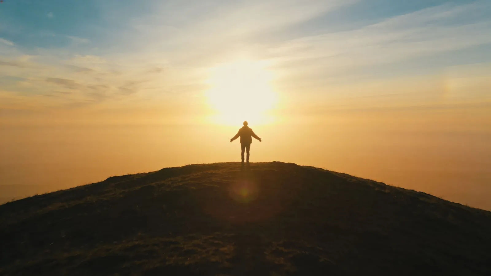 Lone figure on hilltop at glowing sunrise