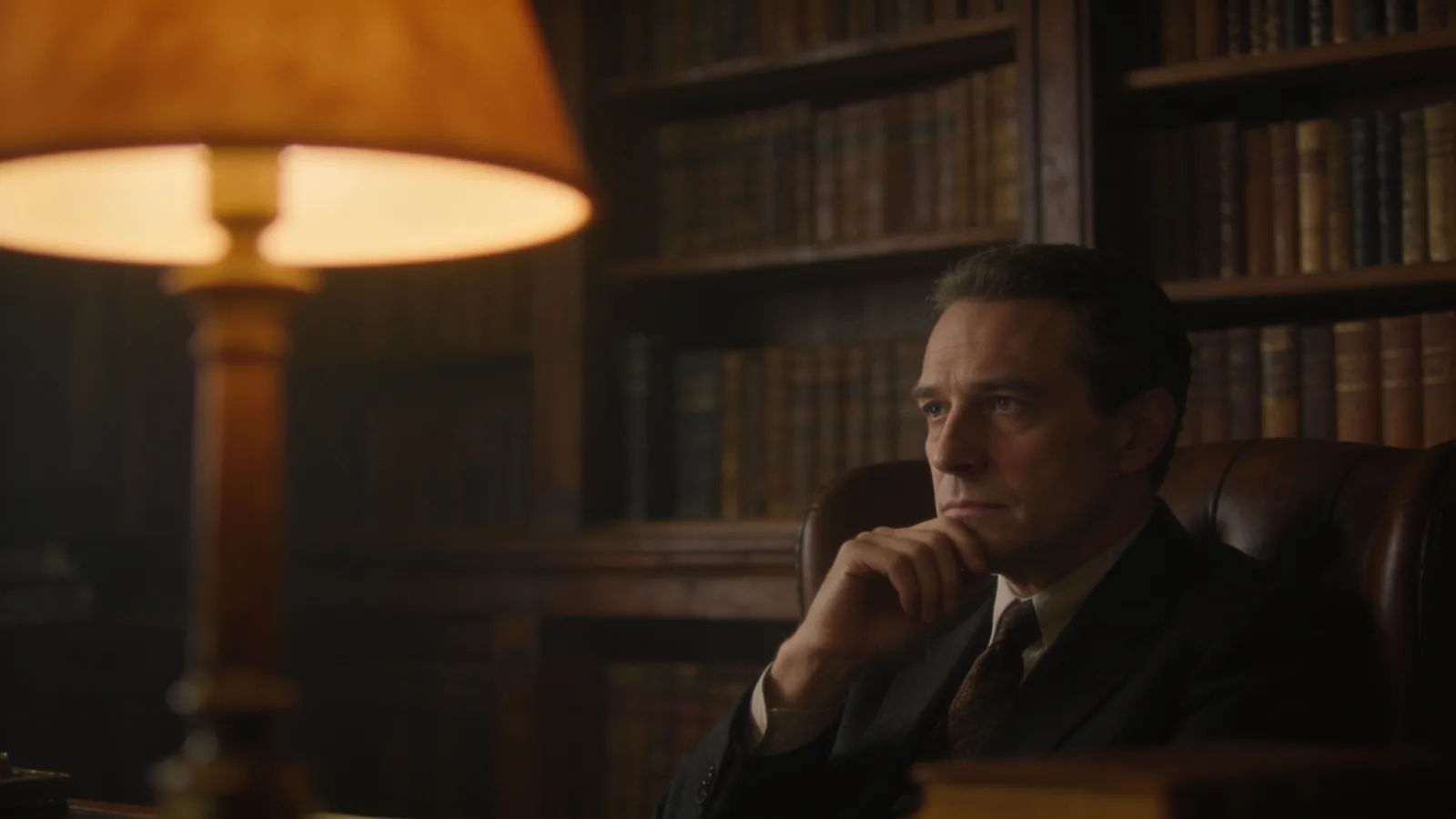 Contemplative scholar in a dim study, warm lamplight