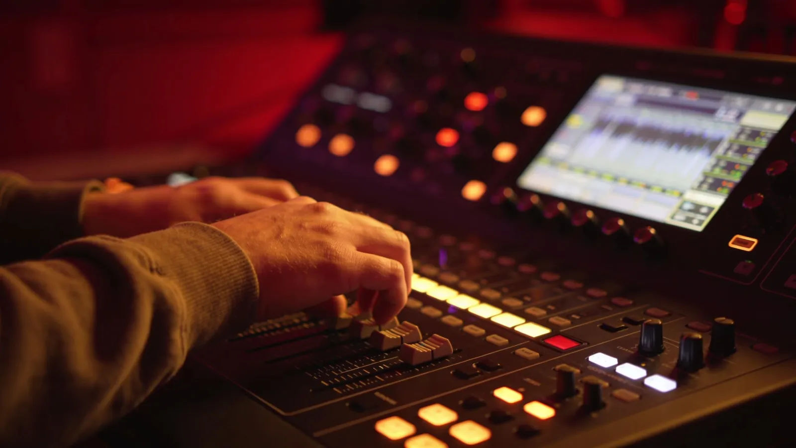 Hands at darkened console with glowing audio controls