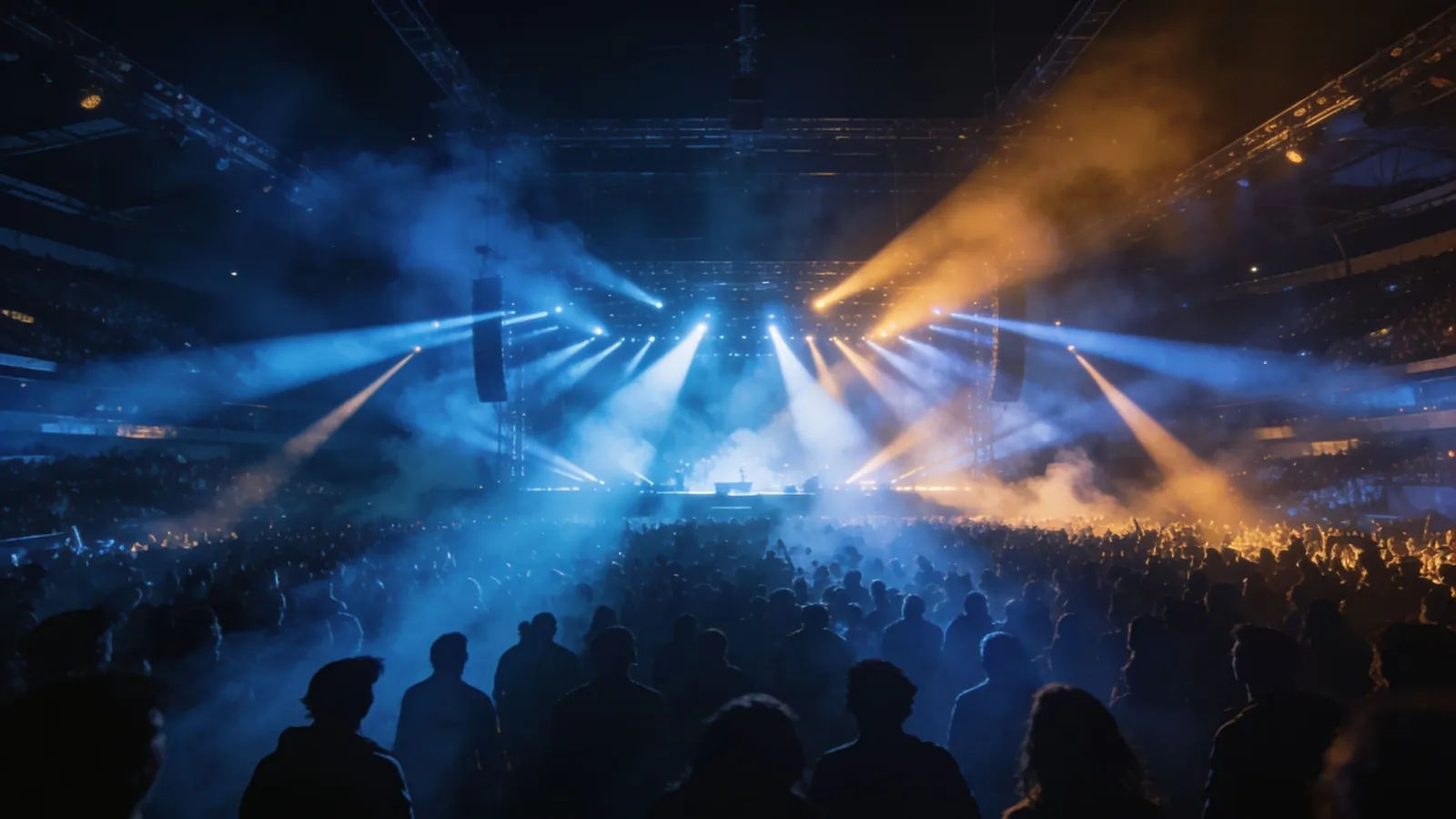 Packed night arena with sweeping stage lights and haze
