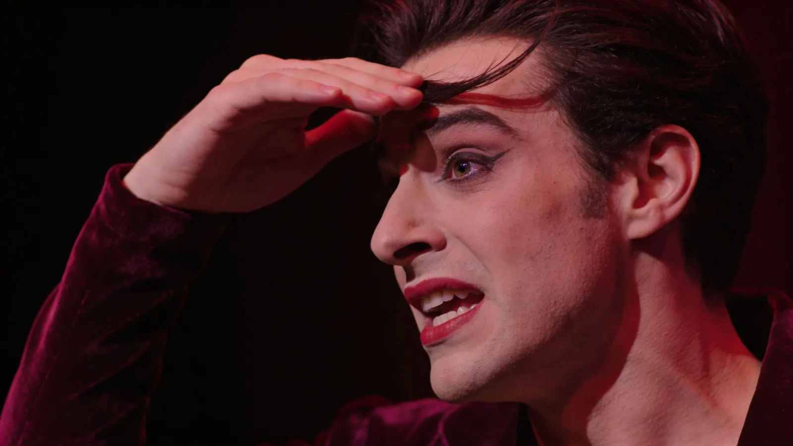 Theatrical figure mid-gesture in crimson stage light