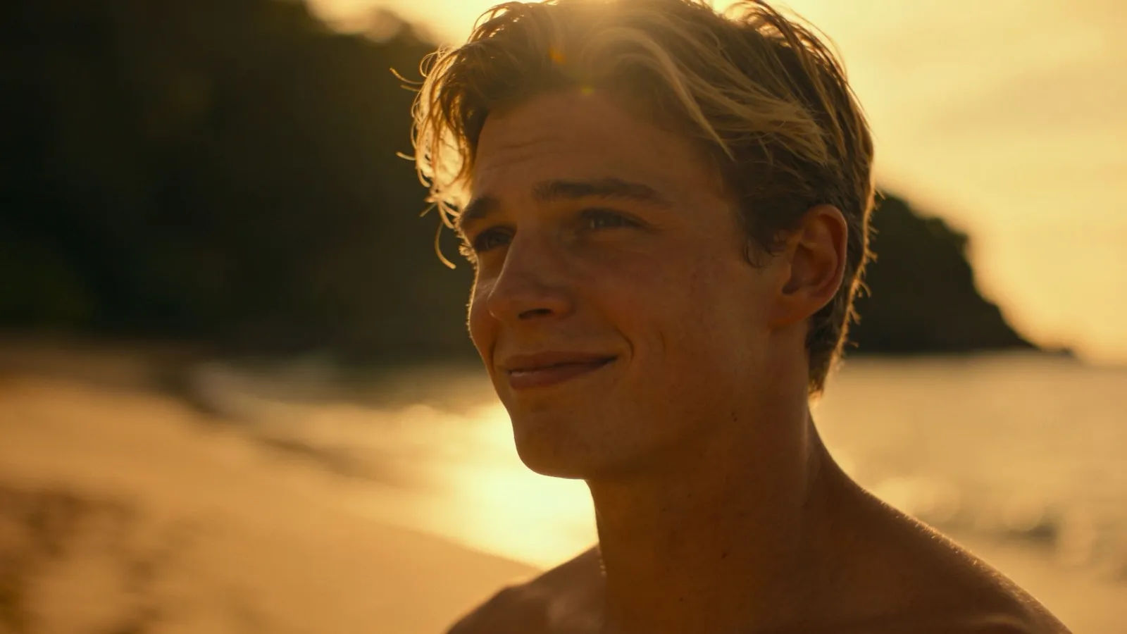 Relaxed sun-bleached young man grinning in beach backlight