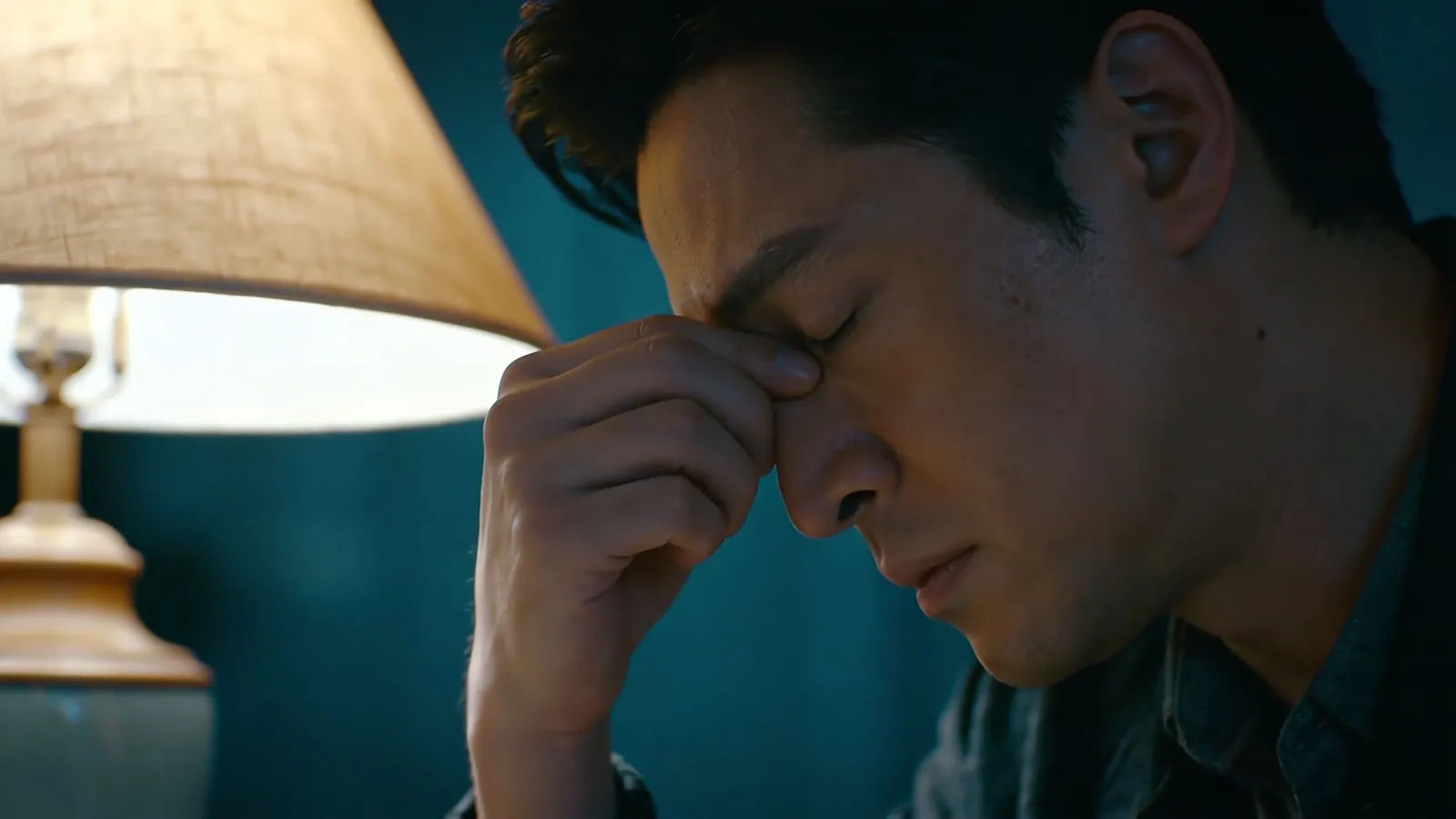 Weary person rubbing eyes under dim lamp