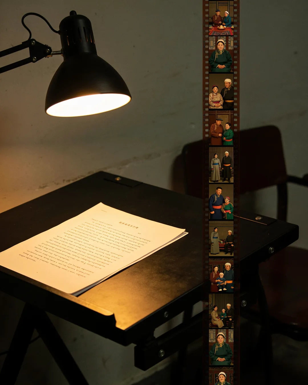A screenplay page under a desk lamp beside a strip of film frames from a Mongolian family drama