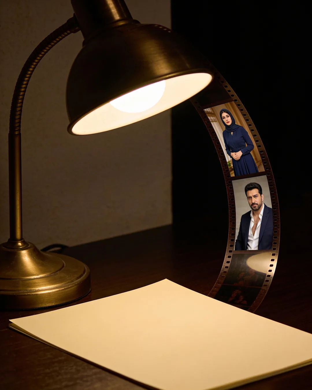 A blank page under a desk lamp beside a strip of film frames from an Arabic family drama