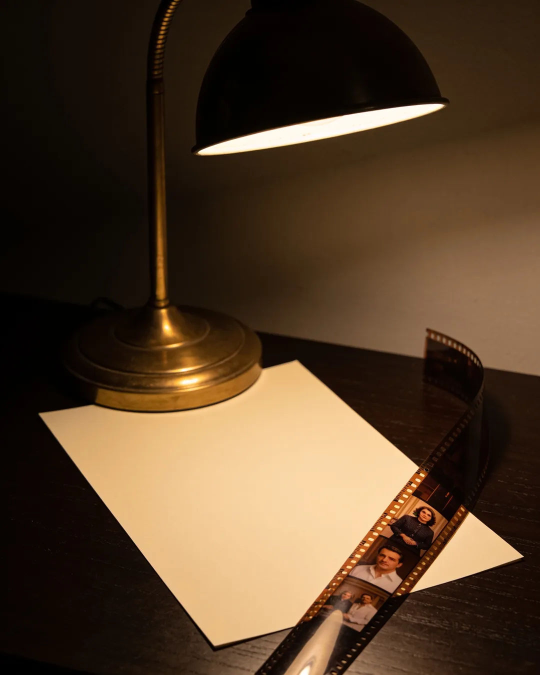 A blank page under a desk lamp beside a strip of film frames from an Italian family drama