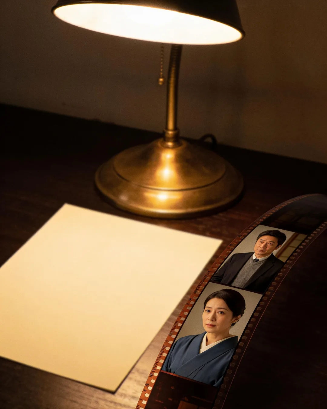 A blank page under a desk lamp beside a strip of film frames from a Japanese family drama