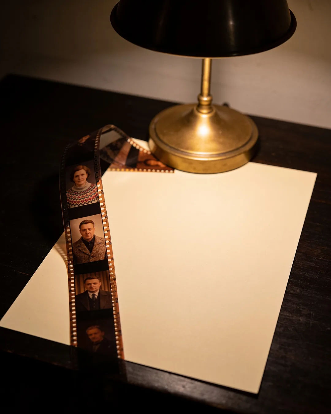 A blank page under a desk lamp beside a strip of film frames from a Polish family drama