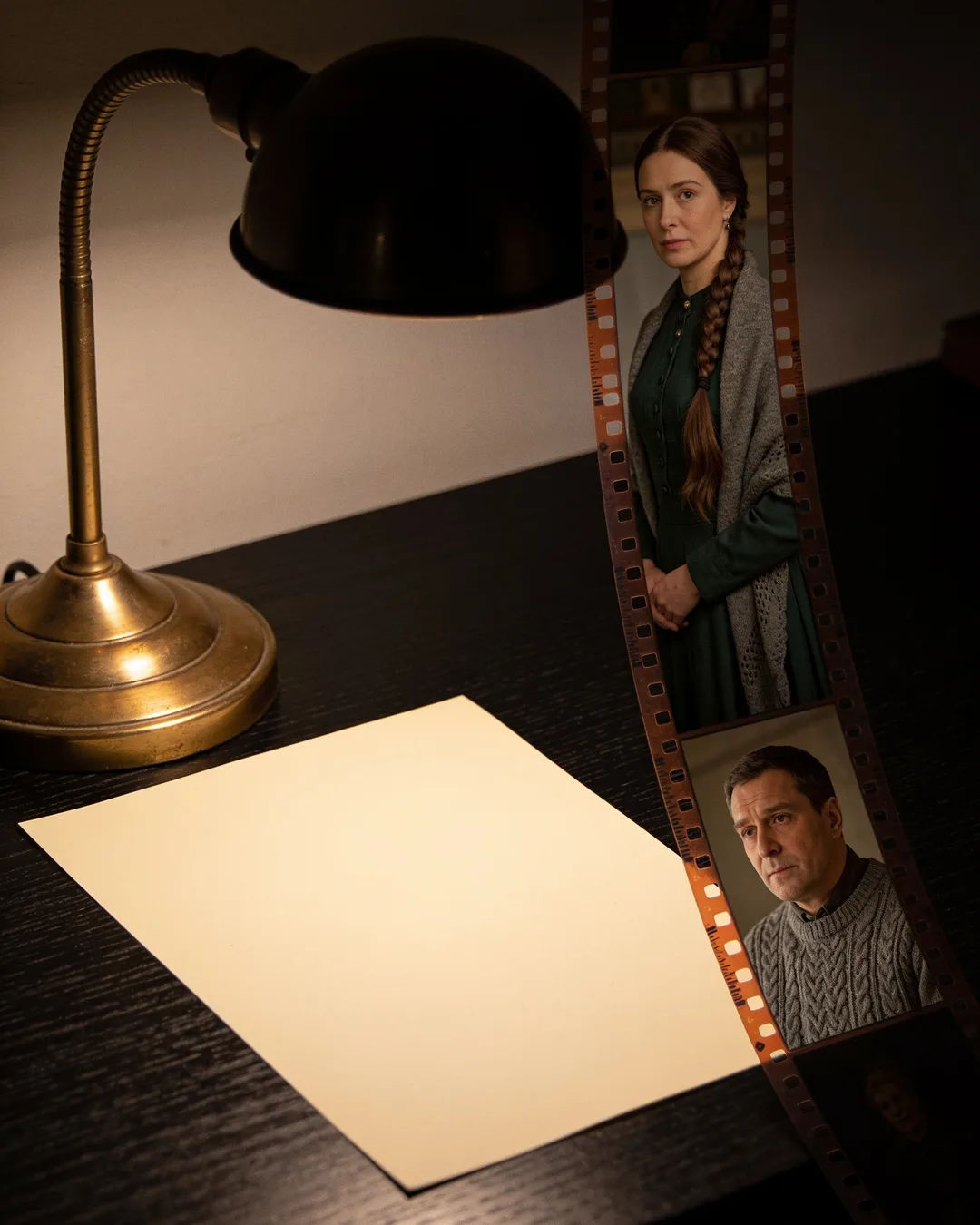 A blank page under a desk lamp beside a strip of film frames from a Russian family drama