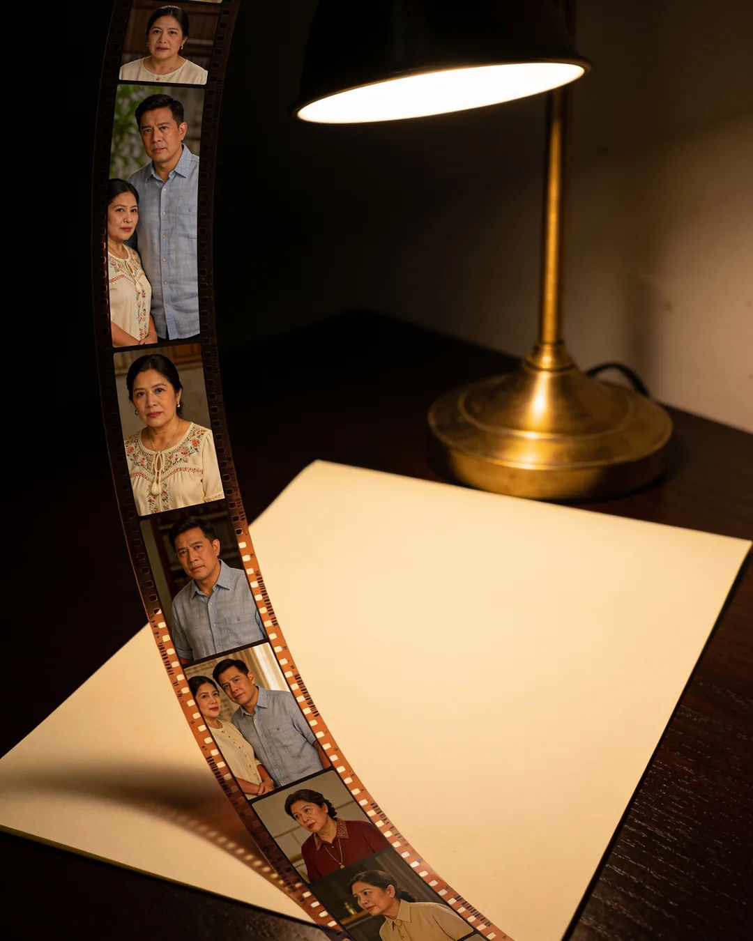 A blank page under a desk lamp beside a strip of film frames from a Filipino family drama
