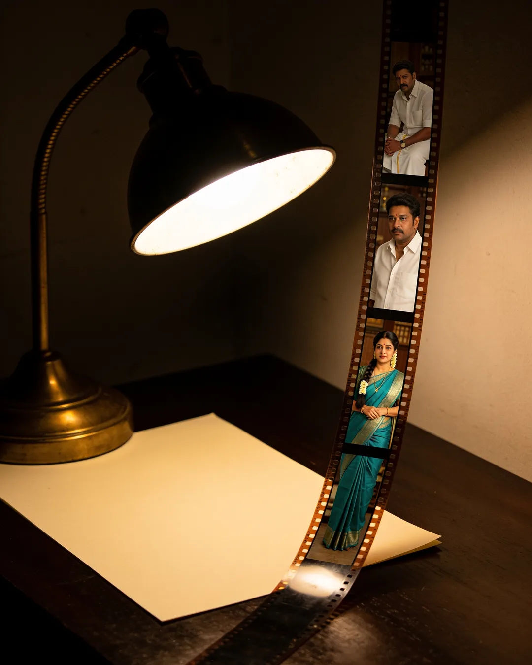 A blank page under a desk lamp beside a strip of film frames from a Tamil family drama