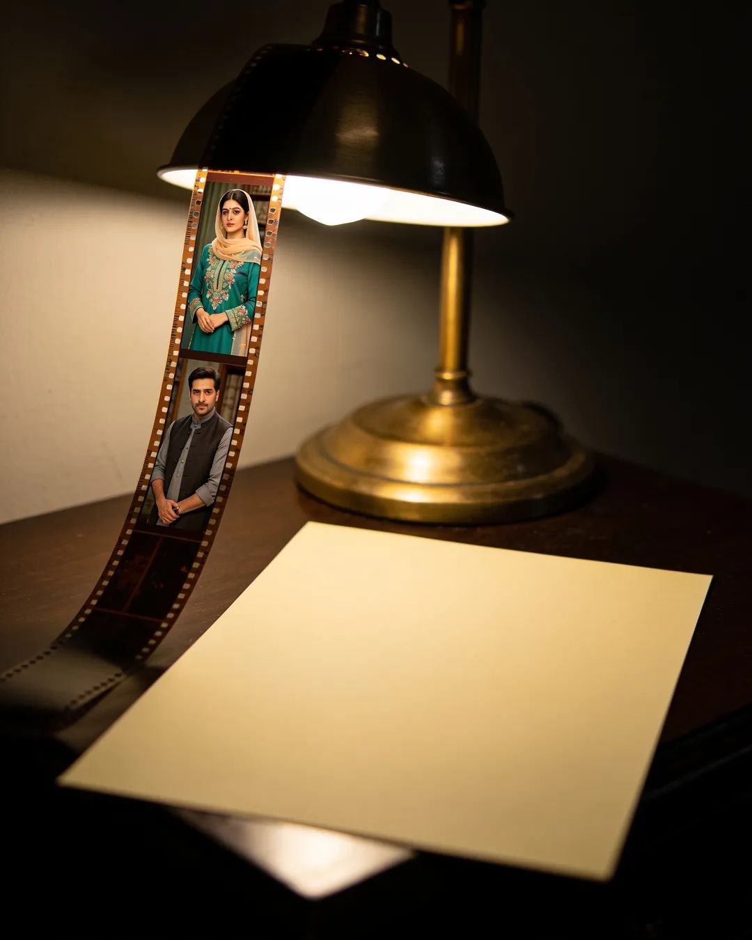 A blank page under a desk lamp beside a strip of film frames from an Urdu family drama
