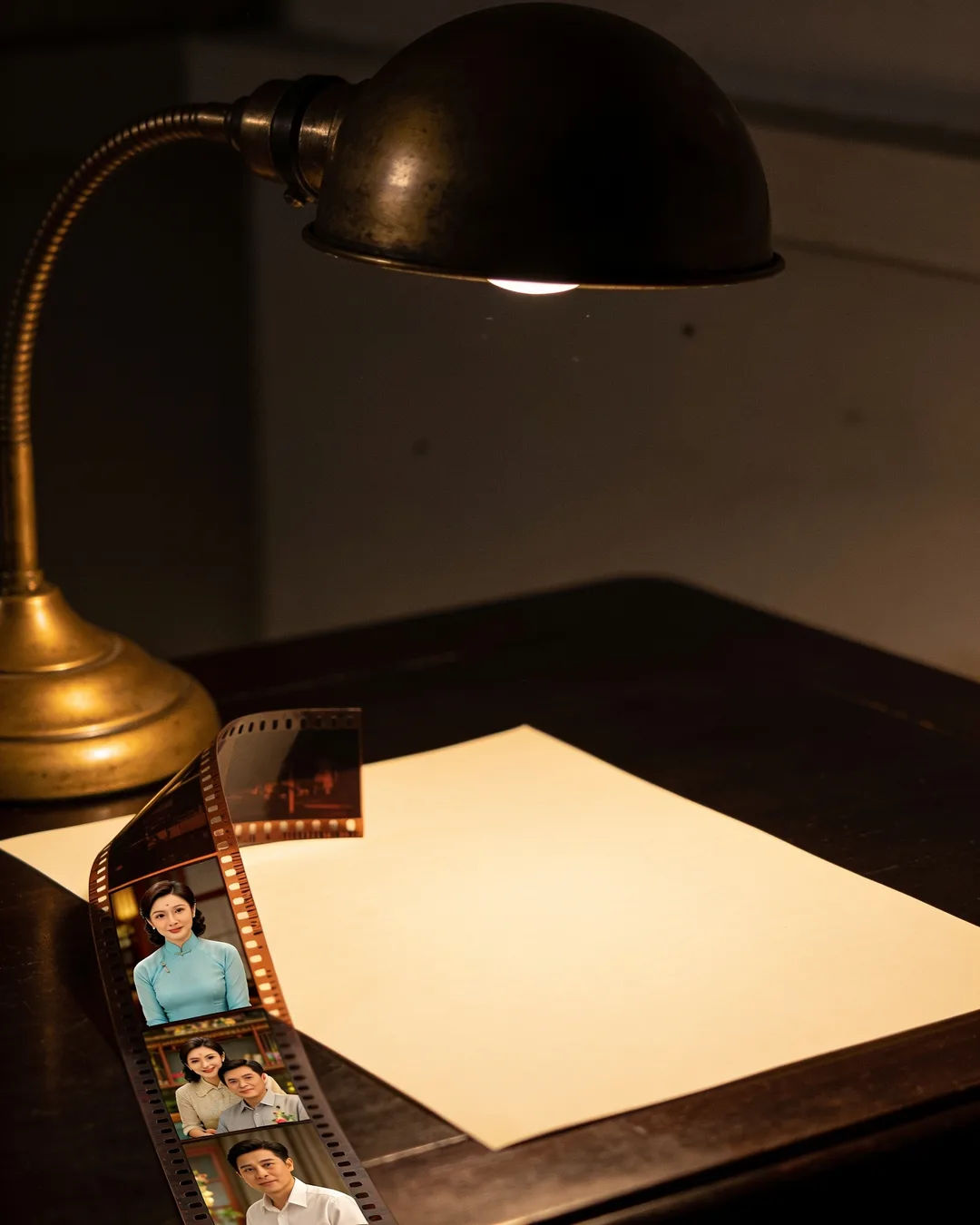 A blank page under a desk lamp beside a strip of film frames from a Vietnamese family drama