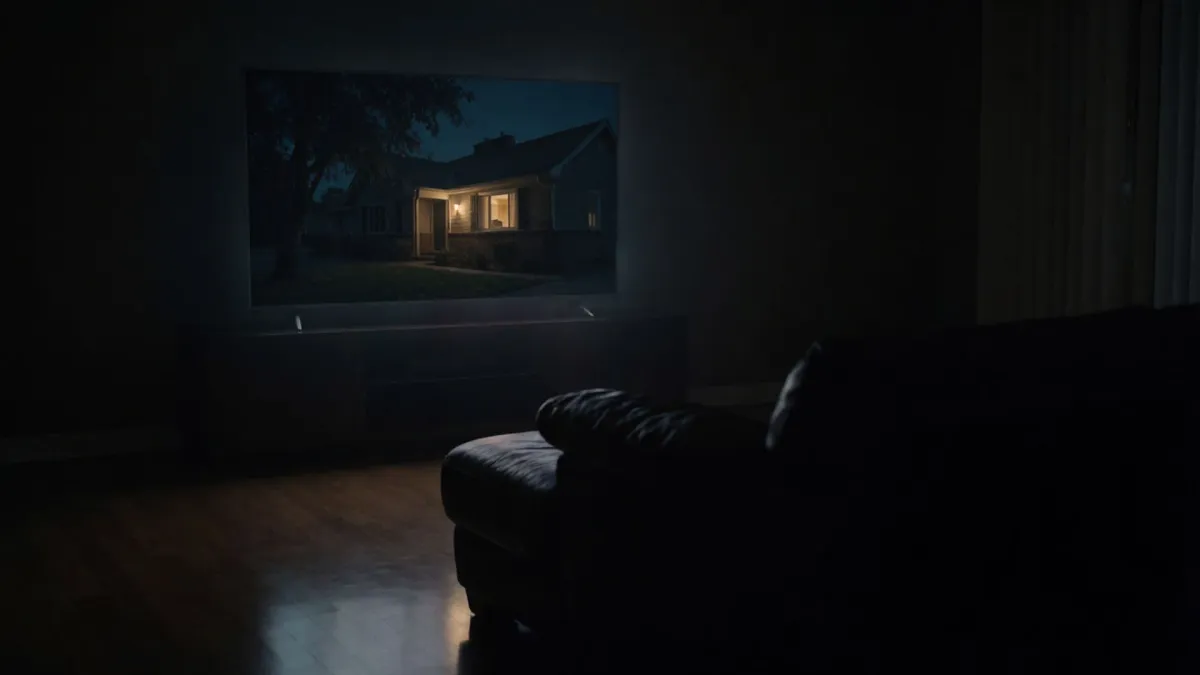 A dark living room lit only by a large television, light spilling across the floor