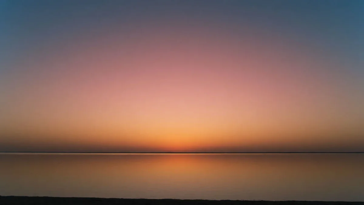 Ein weiter Sonnenuntergang über ruhigem Wasser, vom bernsteinfarbenen Horizont weich ins tiefe Blau darüber