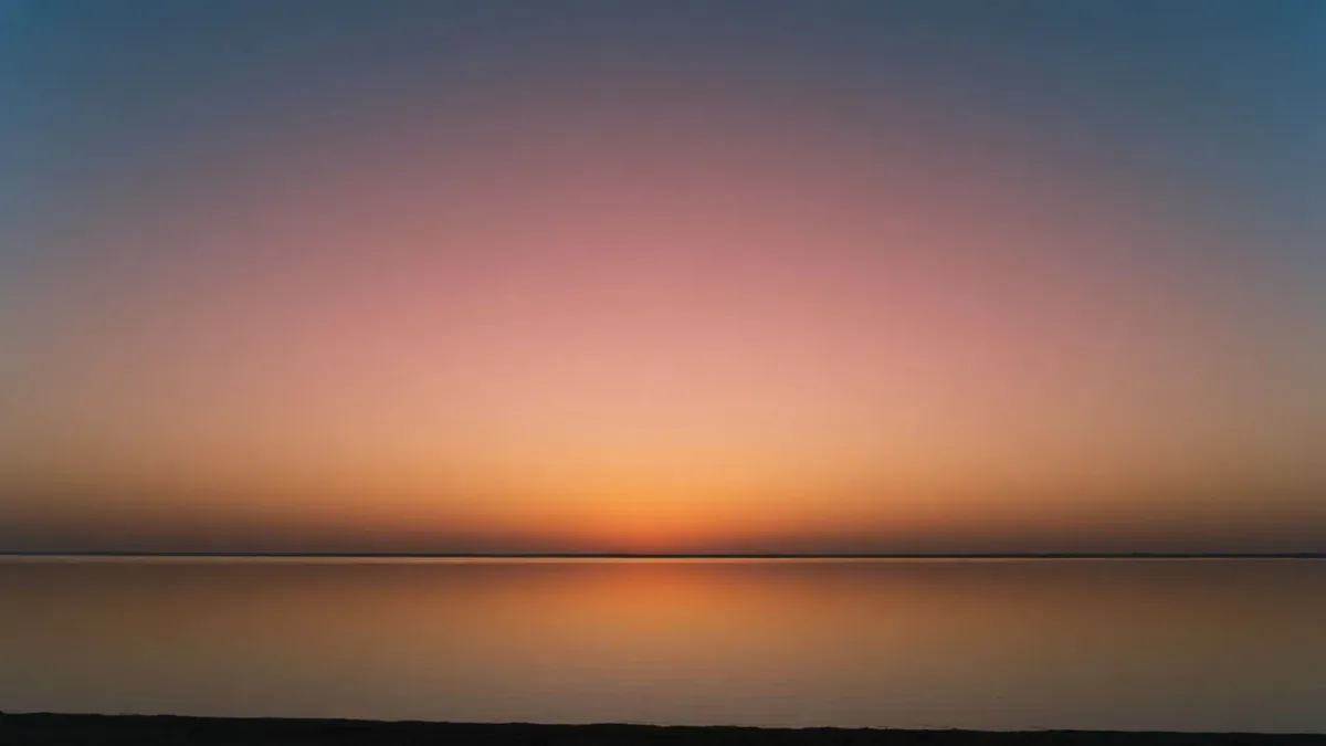 A wide sunset over calm water fading smoothly from amber at the horizon to deep blue overhead