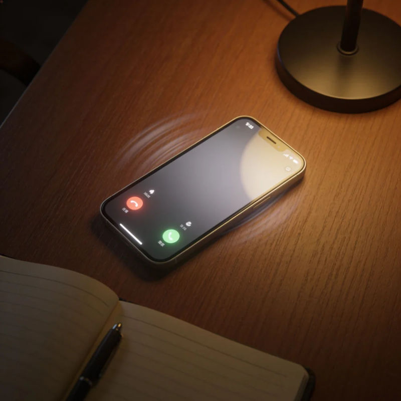 A smartphone lighting up on a wooden desk beside an open notebook