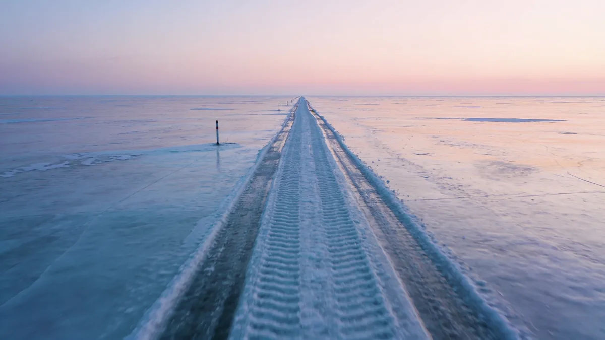 Tire tracks across a frozen lake stretching to the horizon at dawn