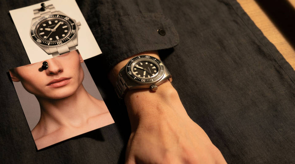 Reference cards of a watch and a model pinned beside the finished campaign frame on dark linen