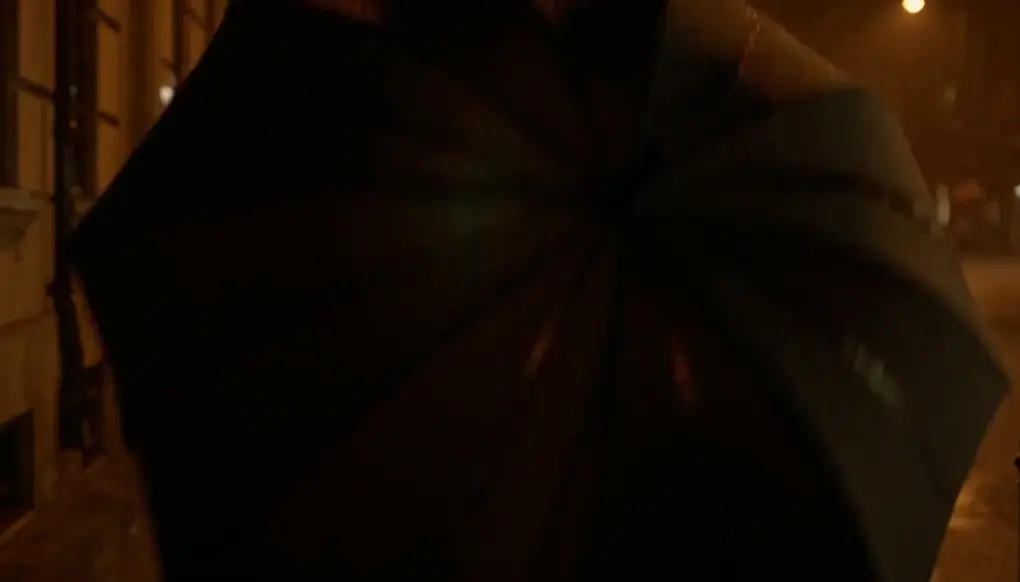 A man opening an umbrella beside a woman on a rainy street at night