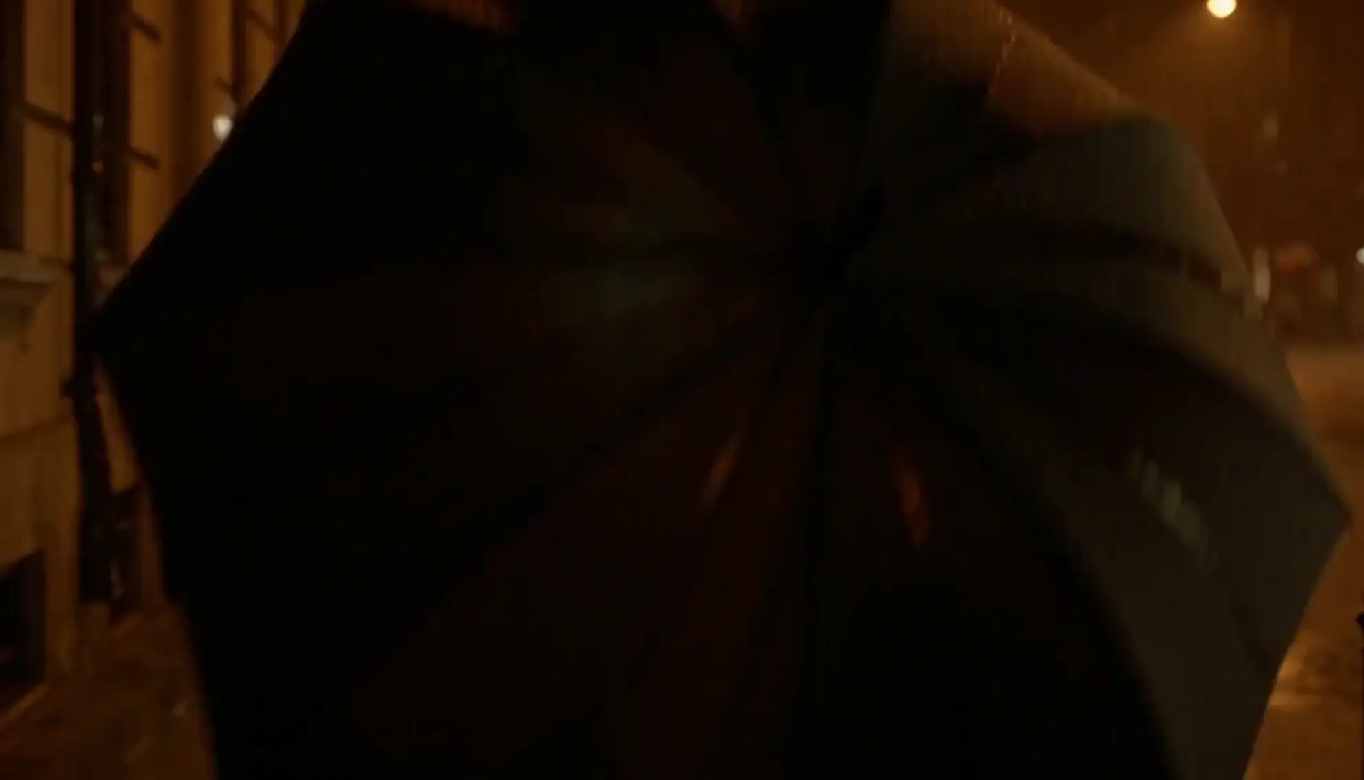 A man opening an umbrella beside a woman on a rainy street at night