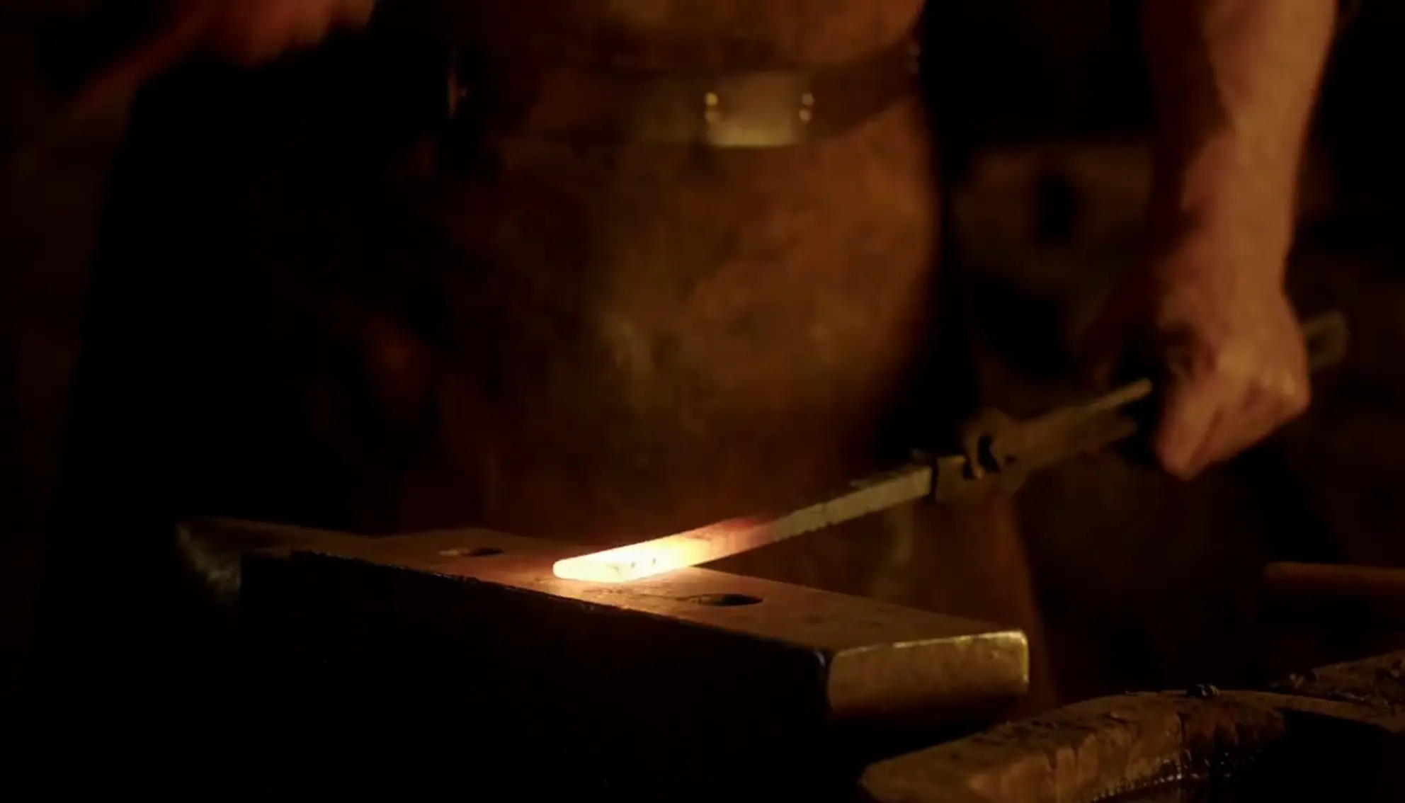 A blacksmith striking a glowing bar on an anvil in a dark forge
