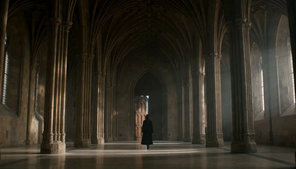 A woman walking across a vast vaulted stone hall in pale daylight