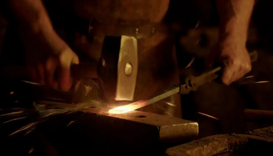 A blacksmith striking a glowing bar on an anvil in a dark forge