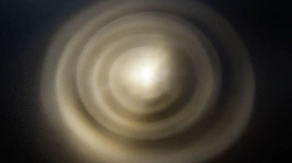 A bright point of white-gold light with soft rings rippling outward