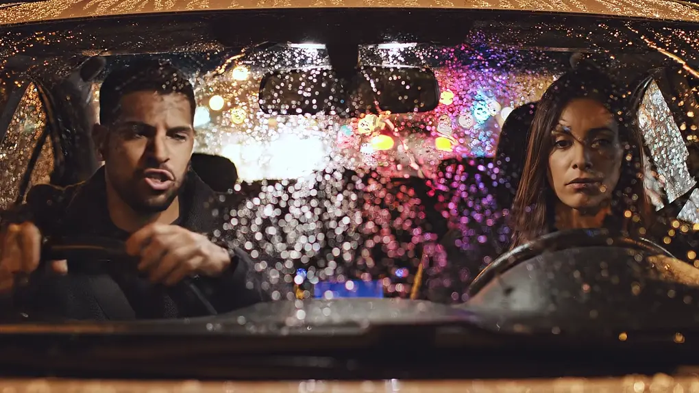 A man and a woman arguing in a parked car at night, rain on the windshield