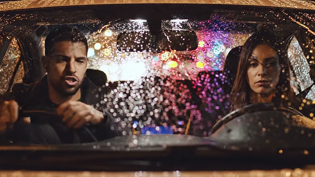 A man and a woman arguing in a parked car at night, rain on the windshield