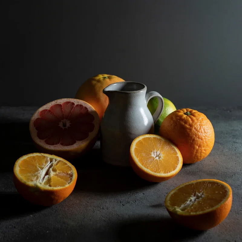 A still life of citrus fruit and a ceramic jug lit by a single softbox against a dark backdrop