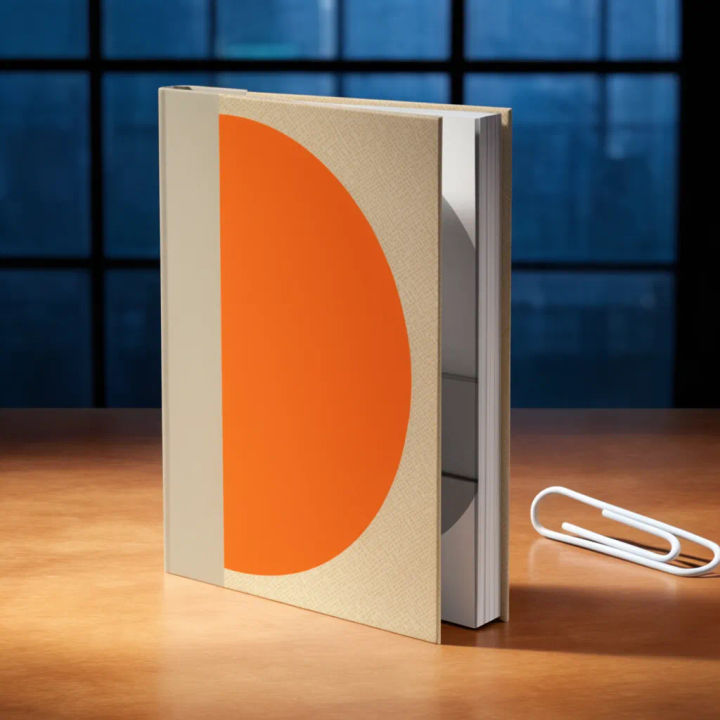 Livro de capa dura em pé sobre uma mesa de madeira com luz quente de janela