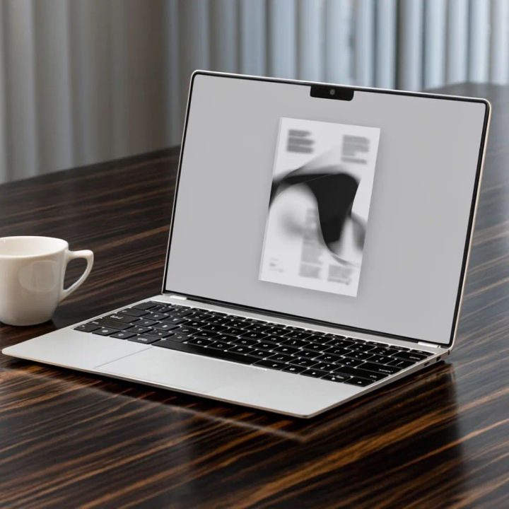 Notebook prateado e fino em uma mesa de madeira organizada com café, exibindo um print