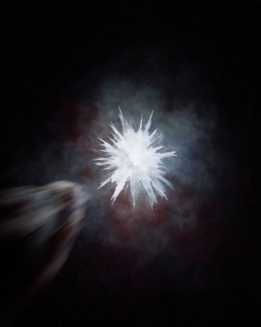 A jagged burst of white light tearing open a pitch black frame with a smeared streak lunging toward the viewer