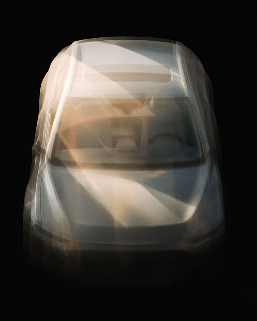 A dim car cabin with warm light sweeping across the dashboard and a road streaming past the windscreen on a black ground