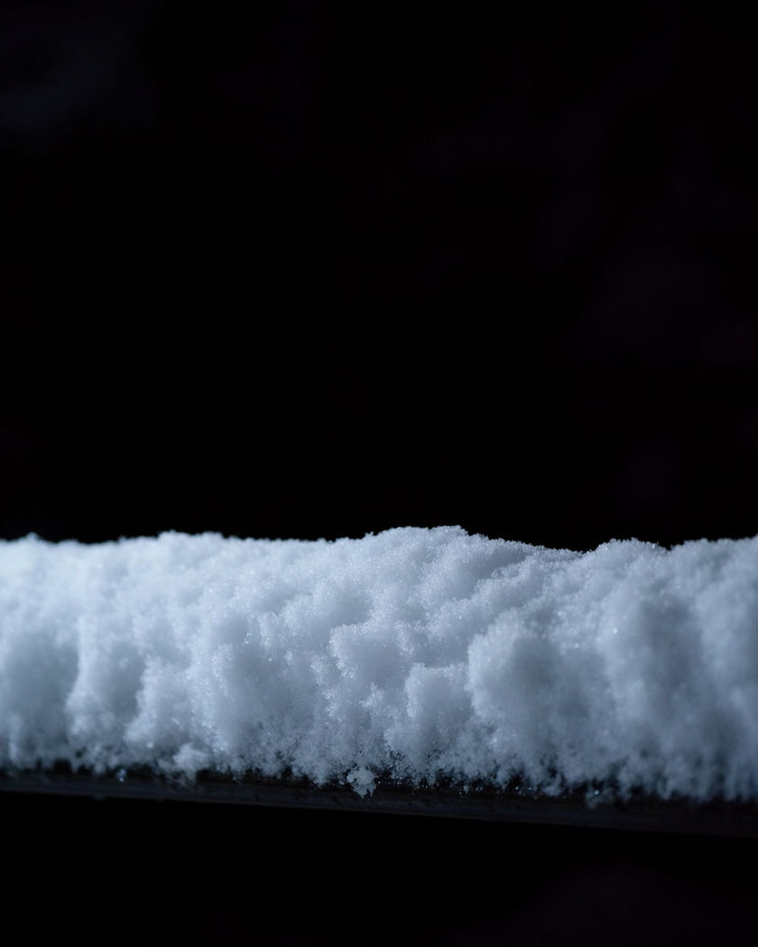 A short horizontal rail with a smooth cap of fresh snow built up along its top on a black ground