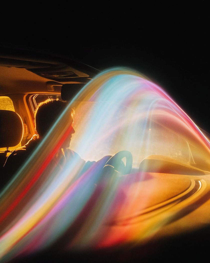 Warm cabin light on a driver while streaks of coloured city light slide across the windshield at night