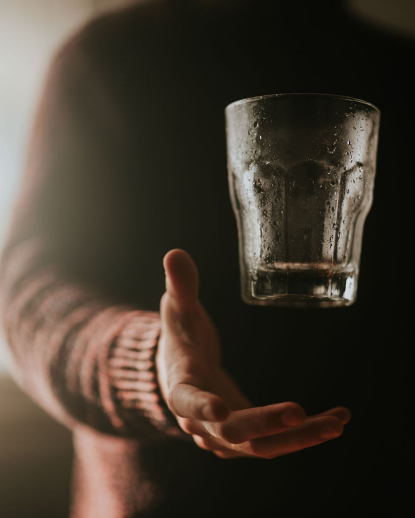 A condensation-beaded glass hovering in mid-air beside a person, catching warm café light