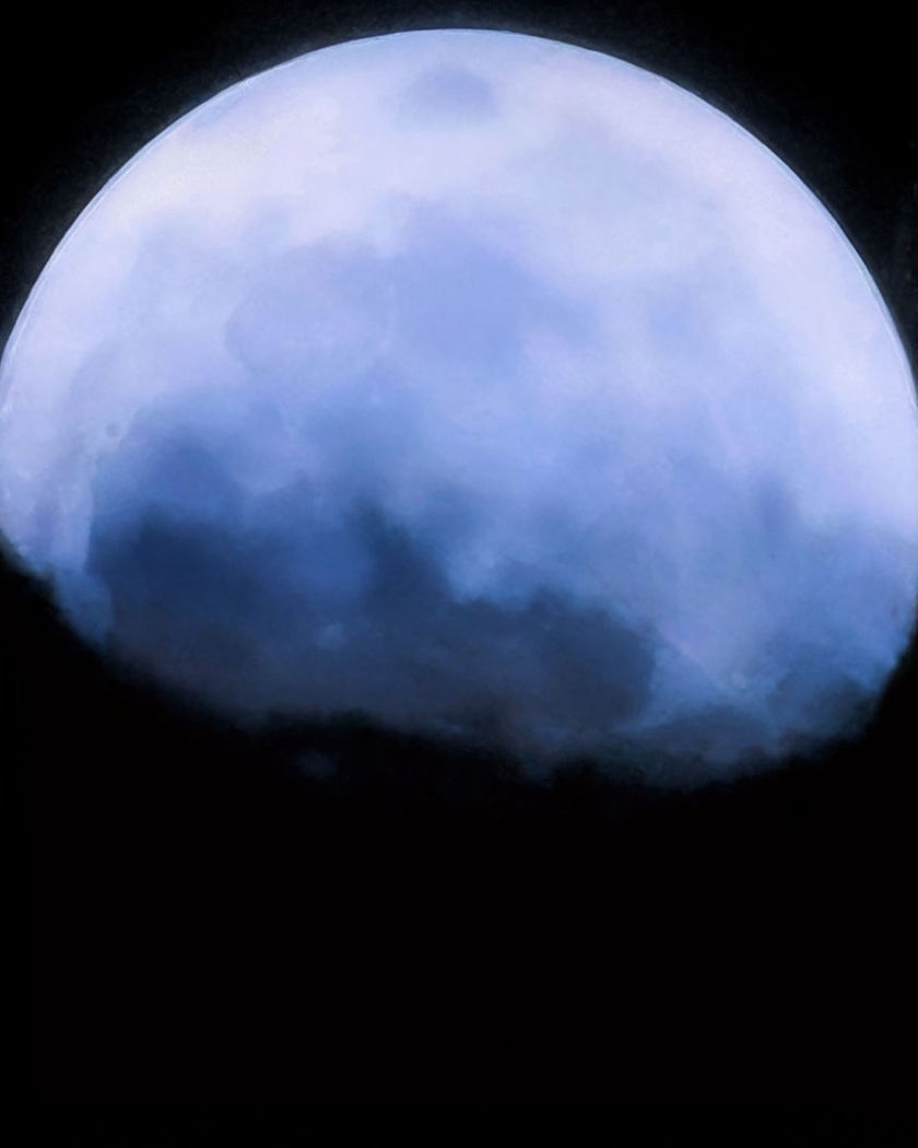 A vast pale moon looming close and low, its cratered surface filling the upper frame over a pure black ground