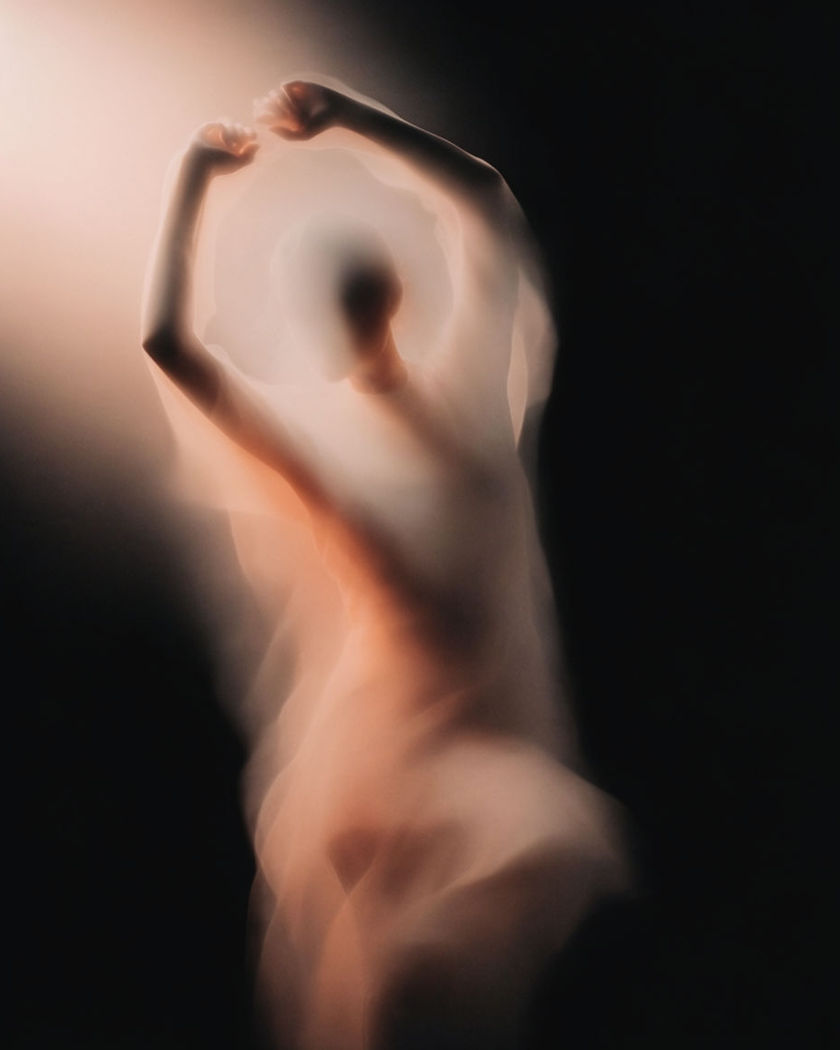 A single silhouetted figure with both arms raised overhead, warm light behind, against a pure black ground