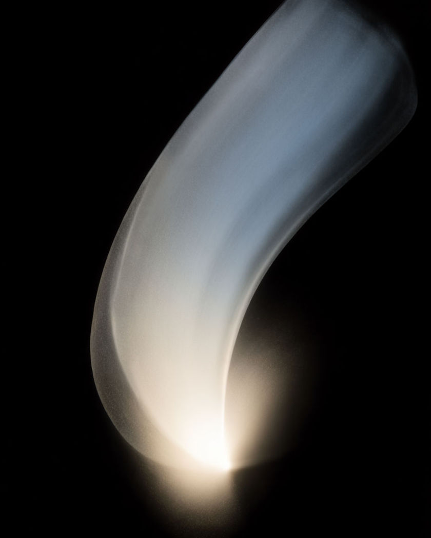 A rising sweep of light opening from a bright point into a widening glow, an unveiling arc against a pure black ground