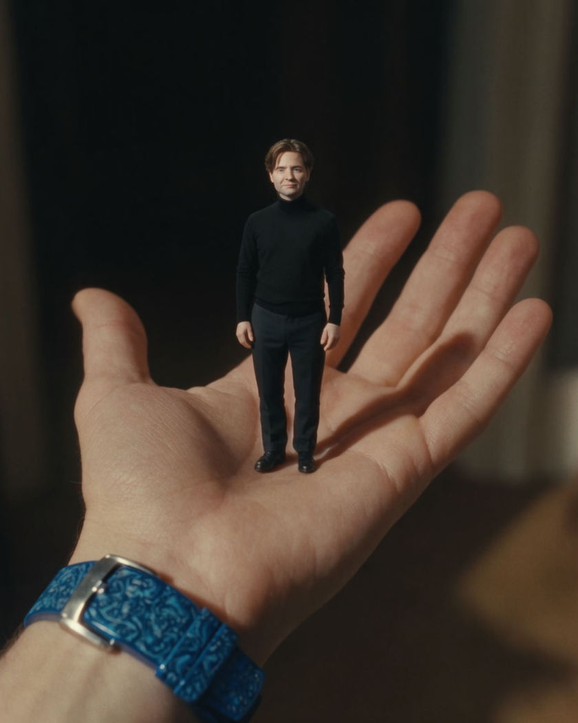 A tiny face-accurate clone of the subject standing on their open palm in a softly lit room