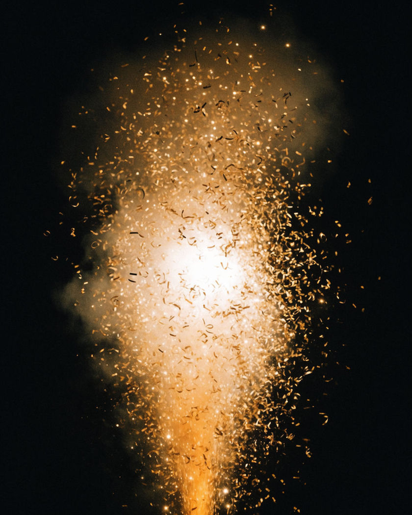 A burst of golden fireworks and drifting confetti sparks rising from a pure black ground, no text
