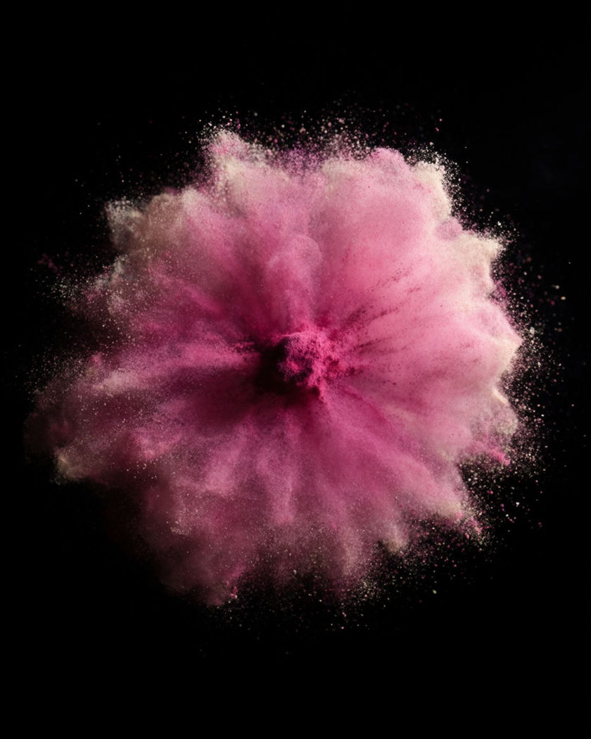 A tight burst of fine luminous pigment exploding outward from a single point at the on a black ground