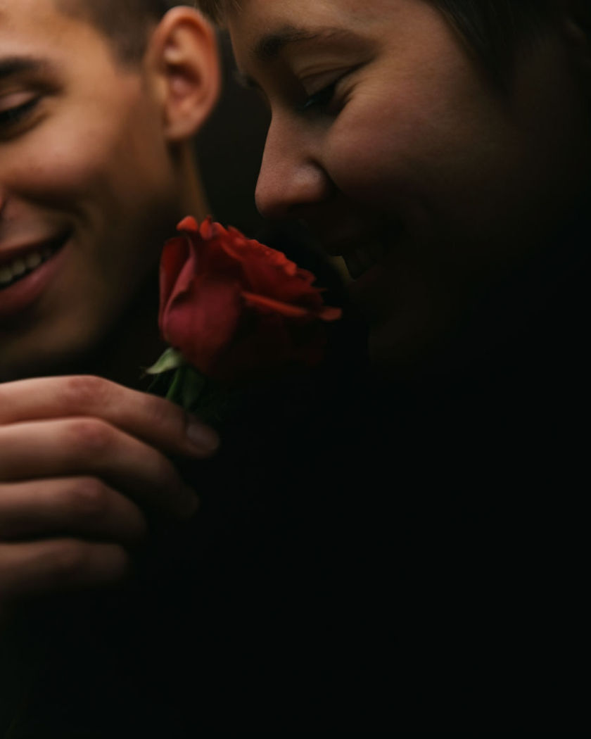 A hand offering a single red rose to another person, both smiling in warm afternoon light